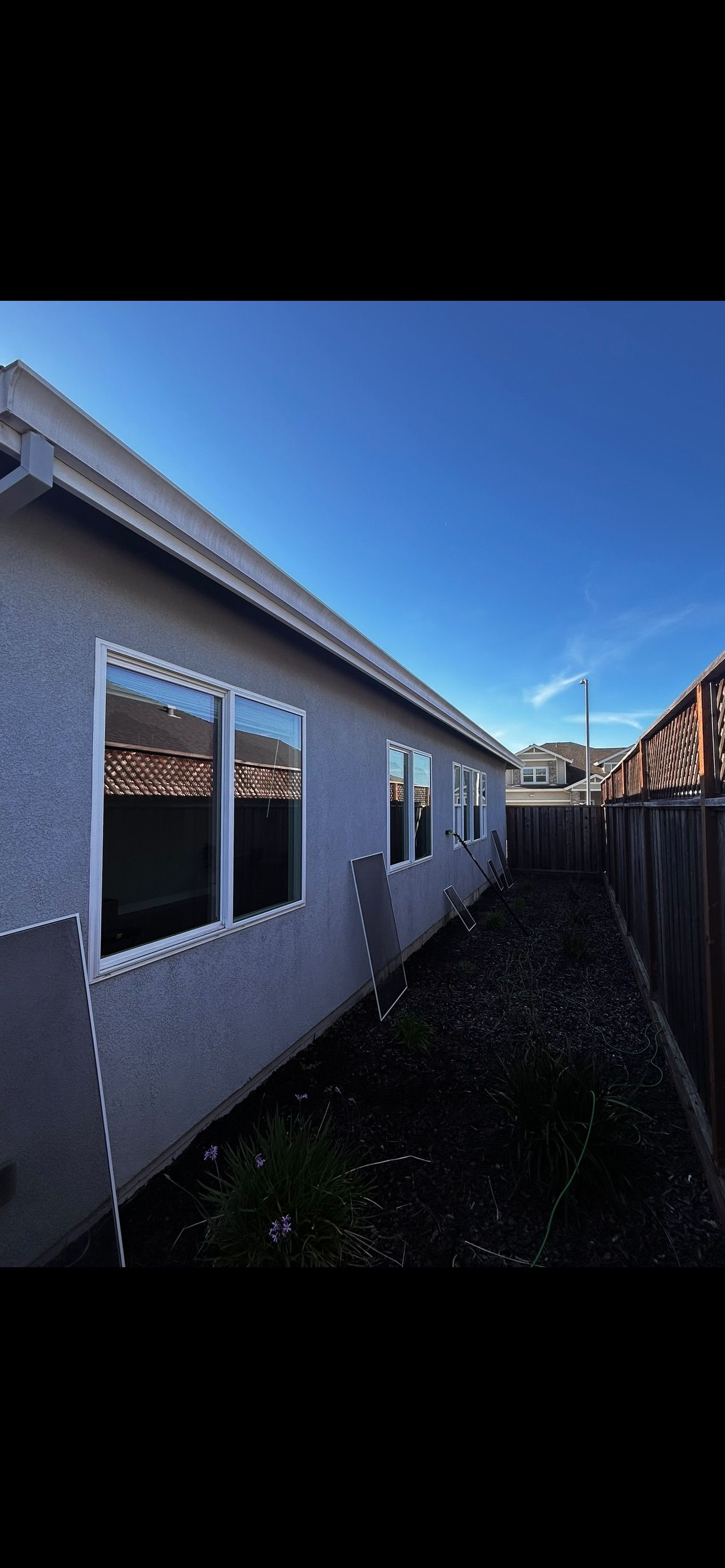 Exterior of a house with a blue sky. Several windows and a wooden fence are visible.