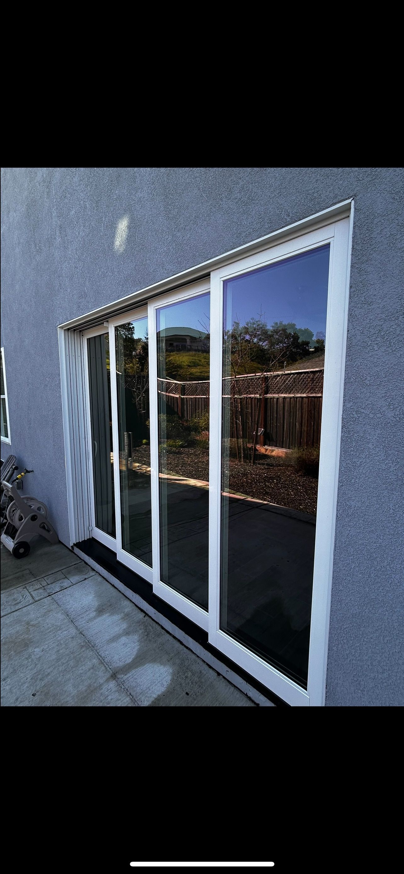 Large sliding glass doors with white frames reflect the outdoors.  The doors are set into a gray textured wall.