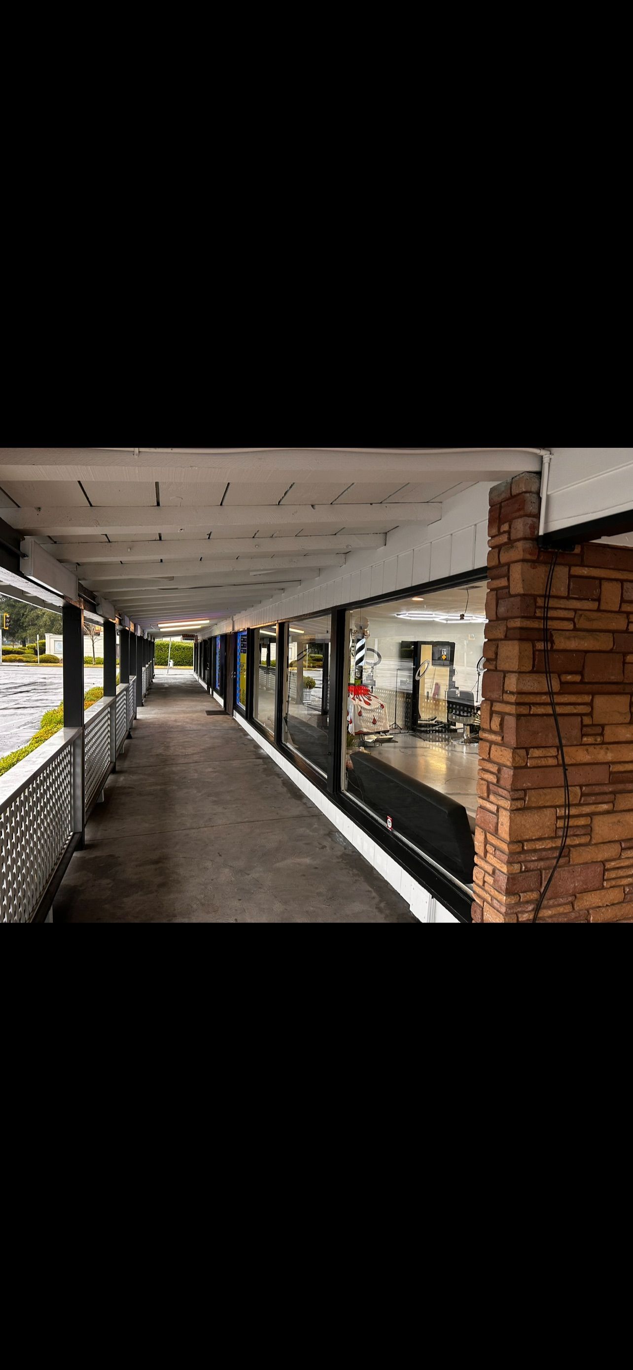 Covered walkway with shops along a strip mall. Brown brick pillar to the right.