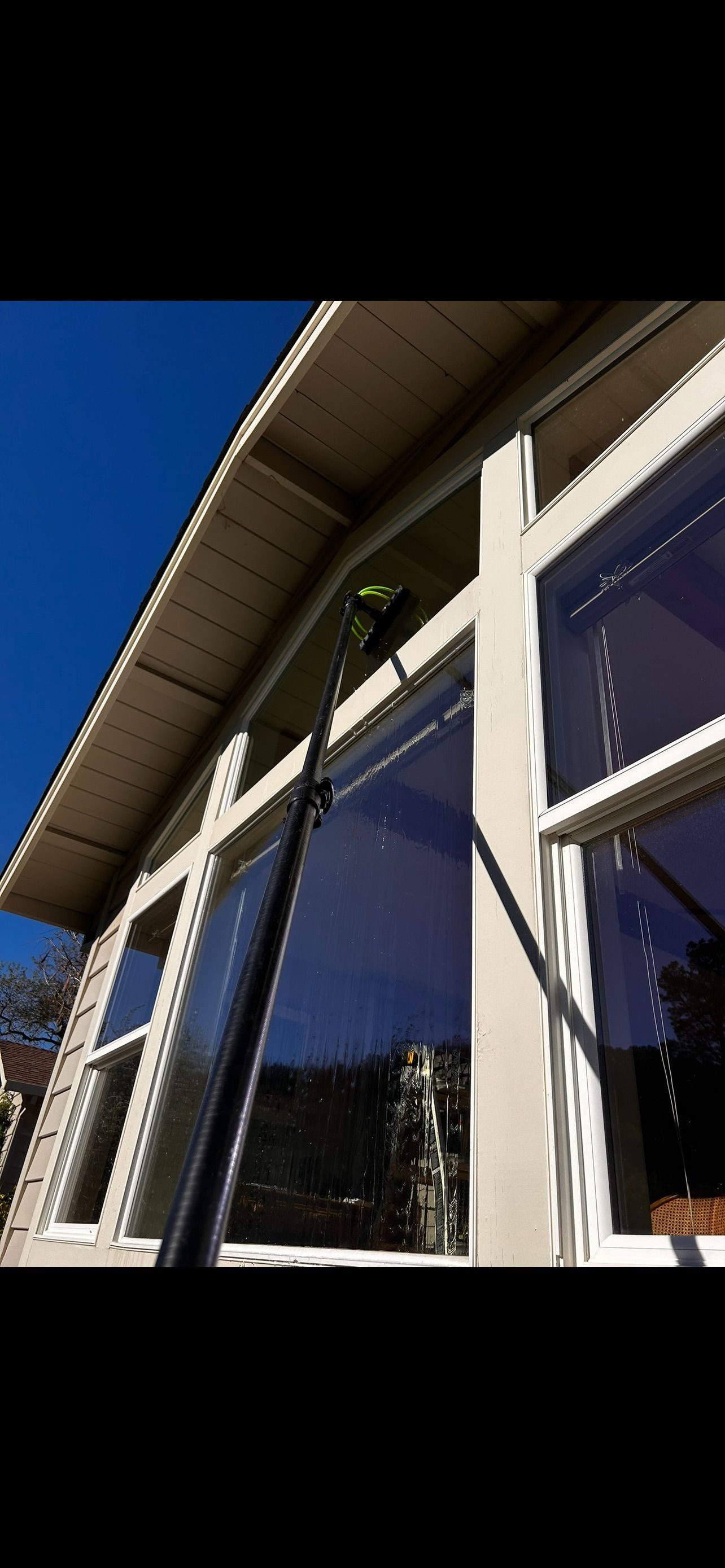 A long pole is cleaning tall windows on a house on a sunny day.
