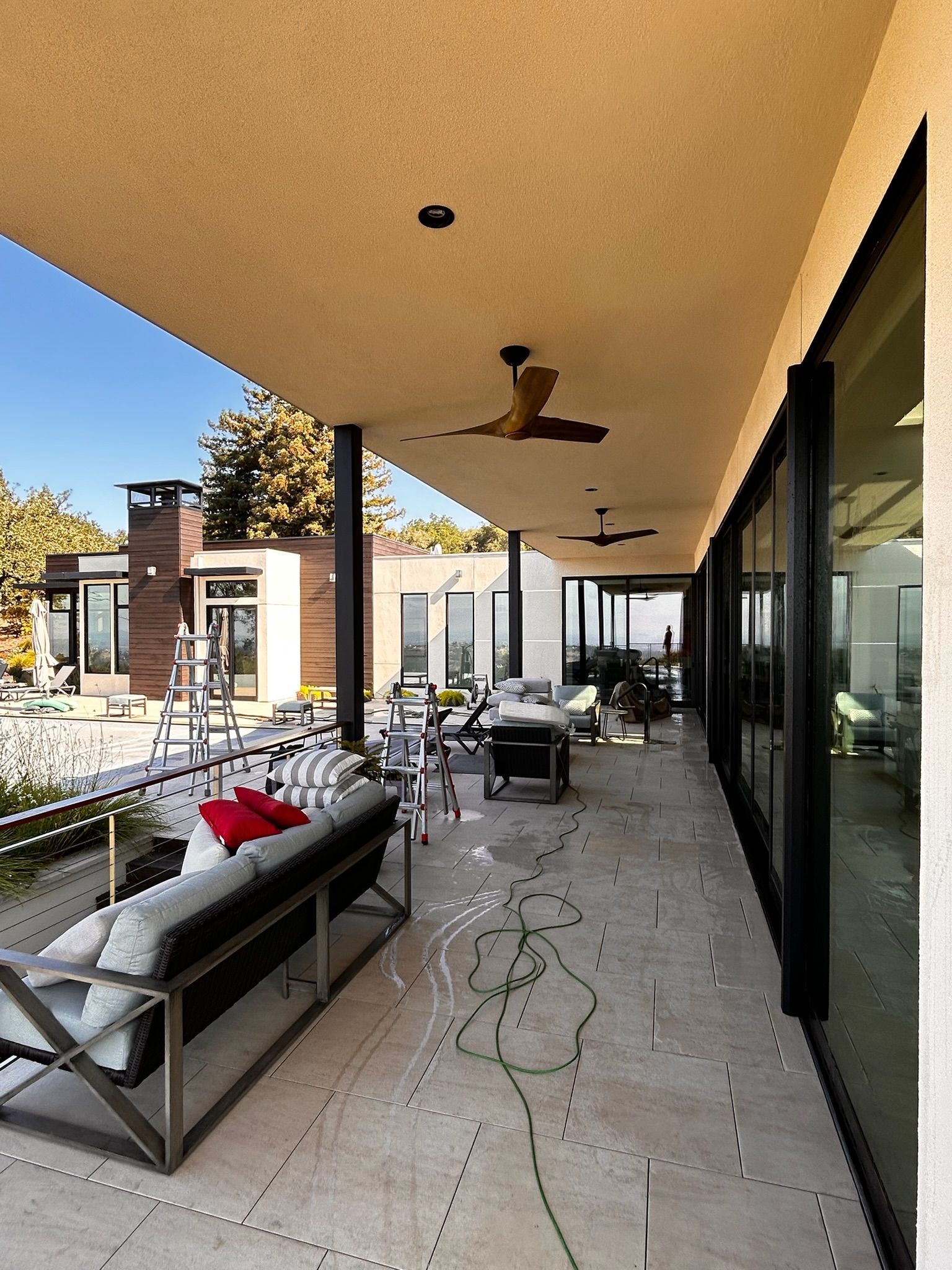Patio with outdoor seating, fans, and view of a modern house, sunny day.