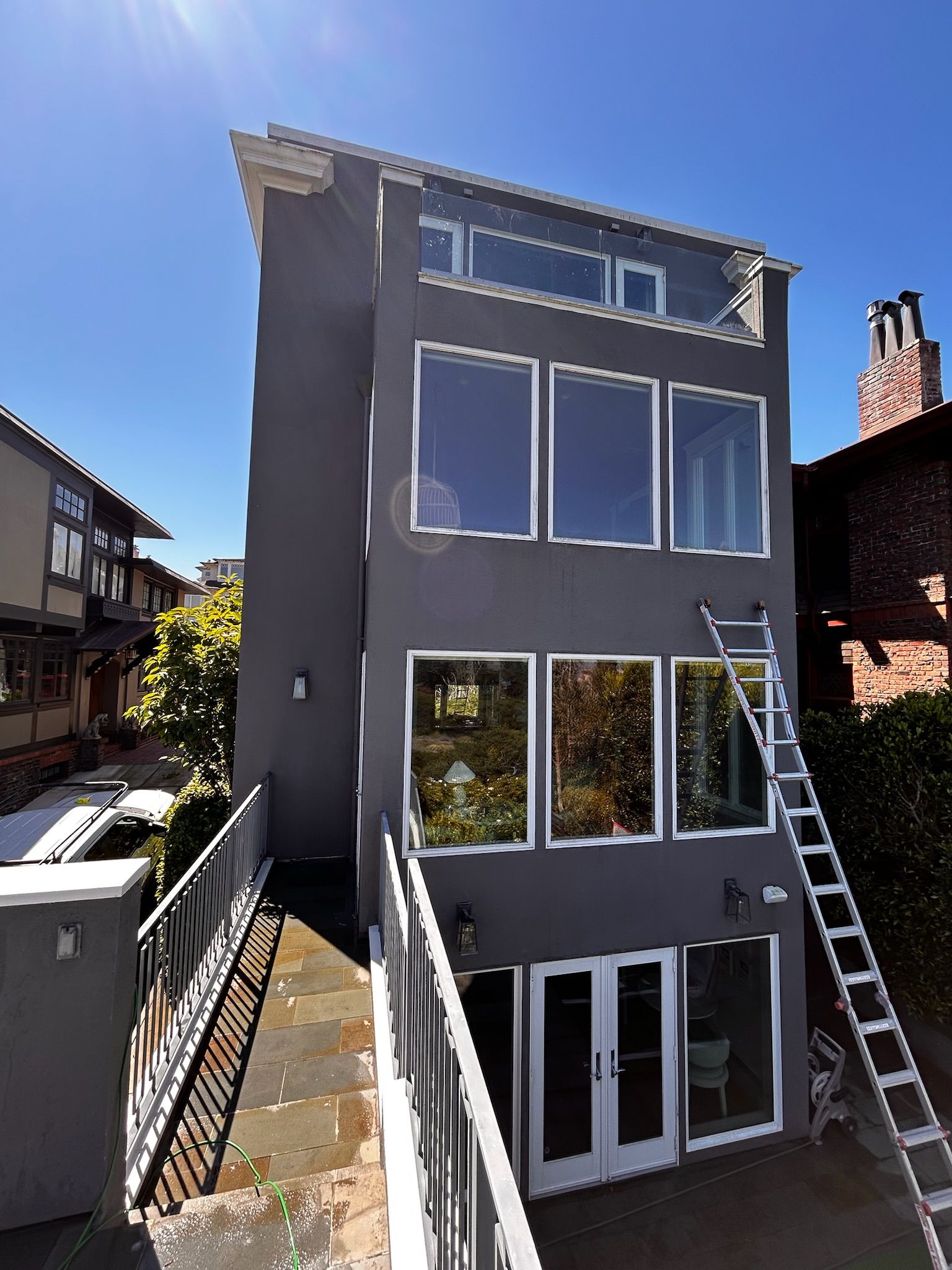 Gray multi-story house with large windows; ladder on the side.