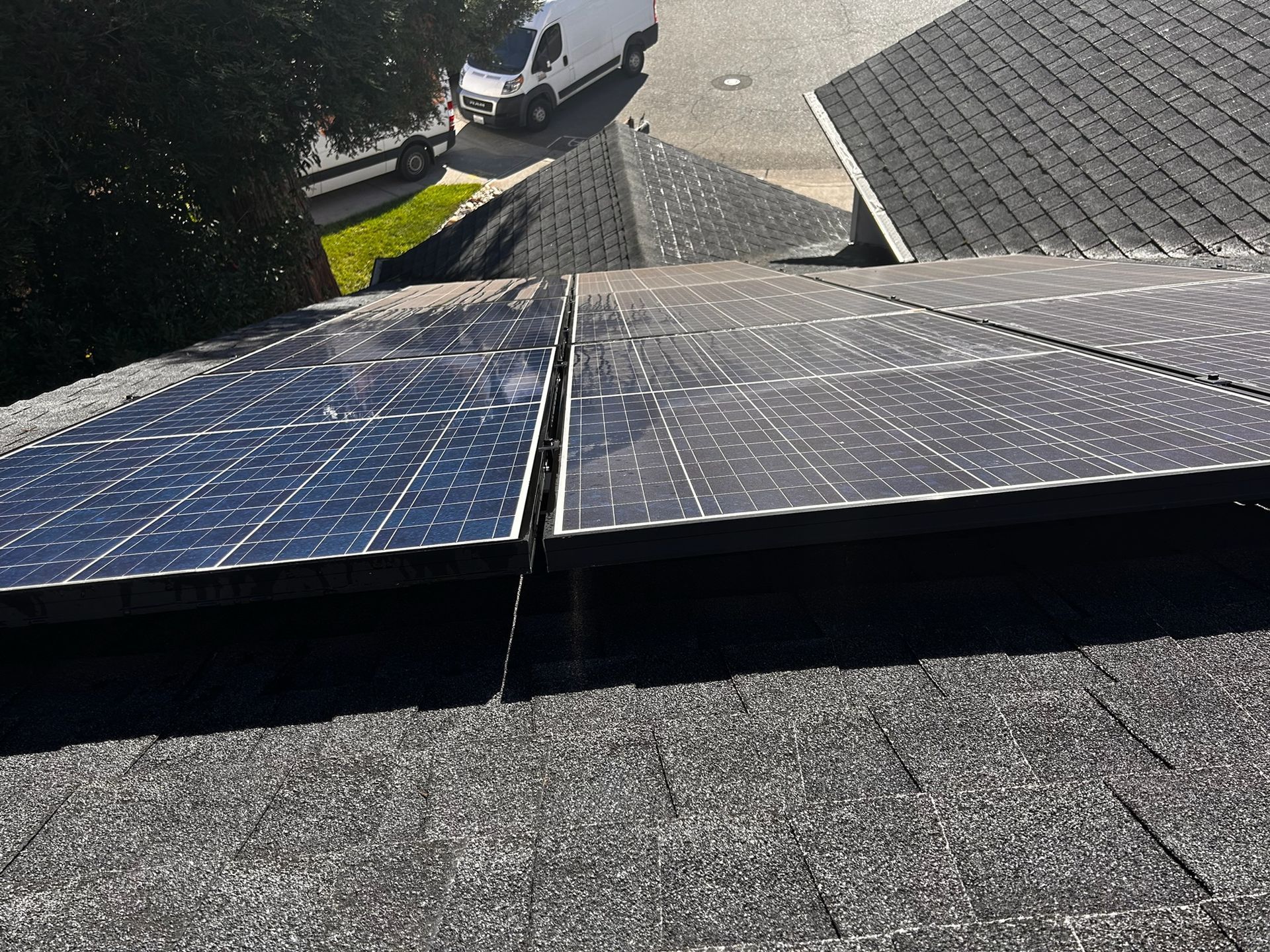 Solar panels installed on a dark gray shingled roof, angled towards a street.