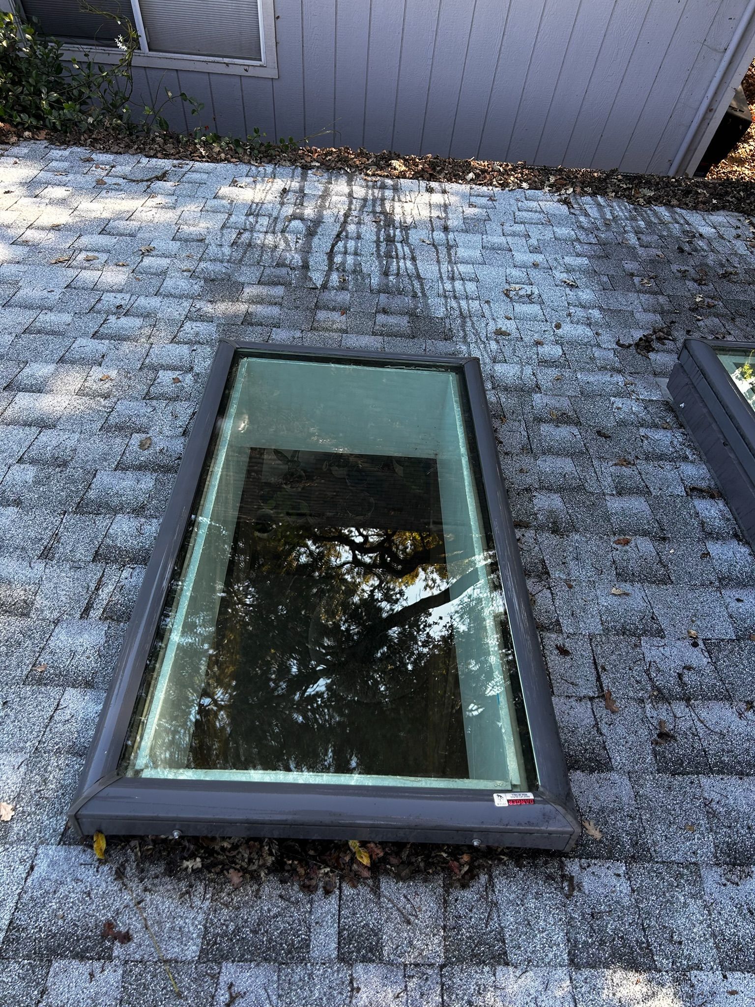 Skylight on a gray shingled roof reflecting trees and sky.