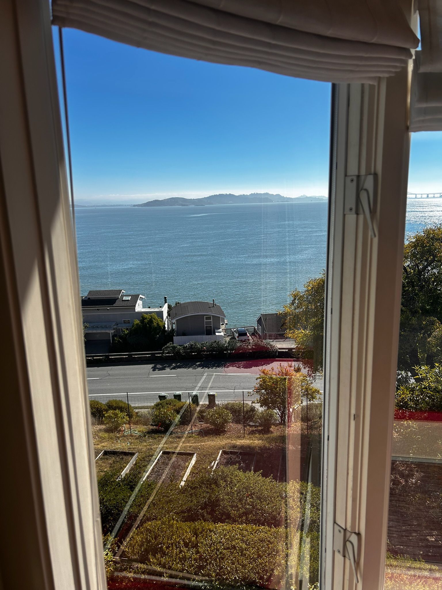 View through a window overlooking the ocean and distant island under a blue sky.
