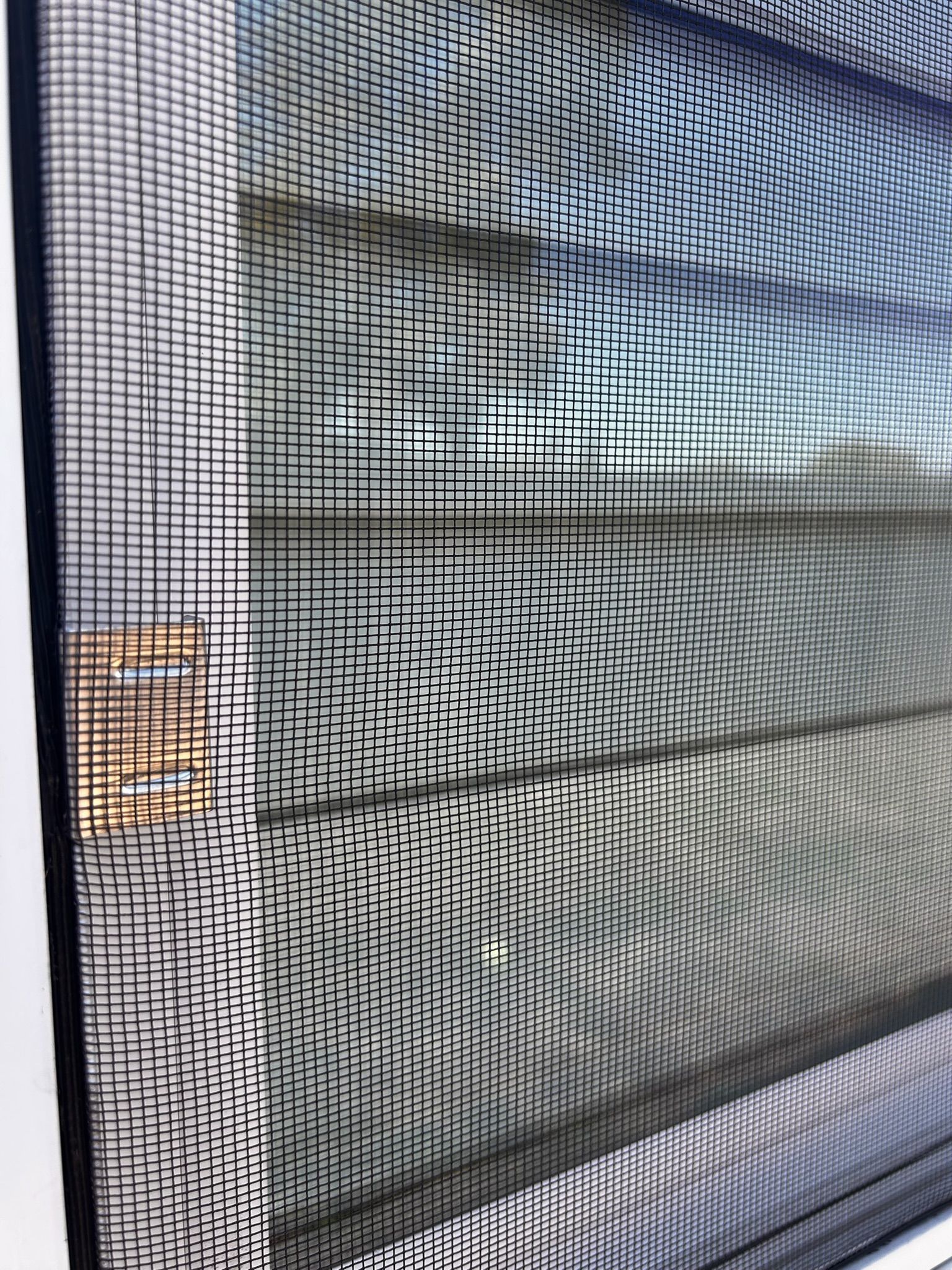 Close-up of a window screen, showing a grid pattern with the blurred view of a building in the background.