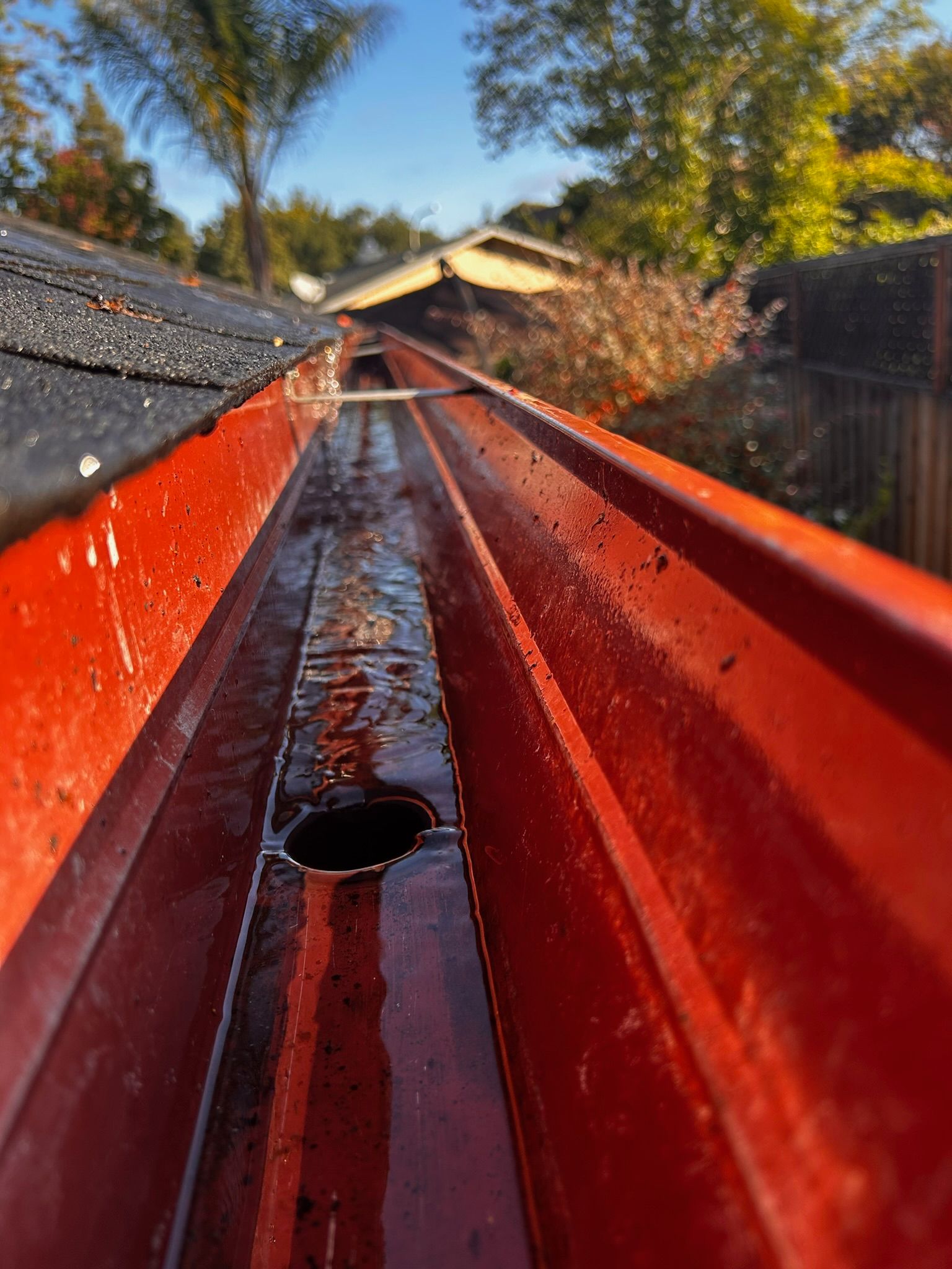 Red gutter with water and debris, viewed from inside, under a dark roof.
