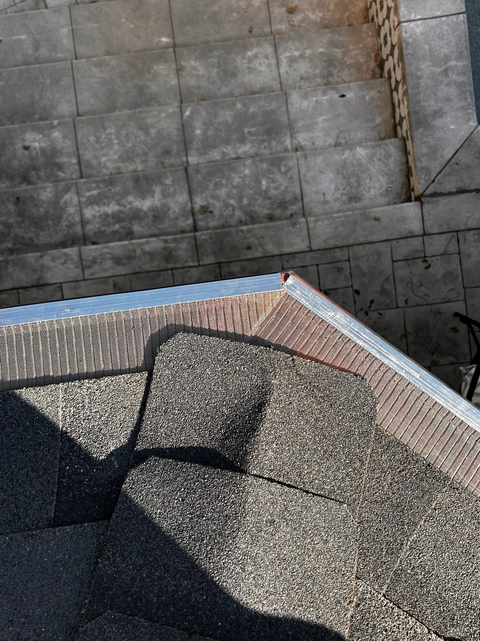 Overhead view of a roof corner with brown shingles, metal flashing, and stone steps leading down.