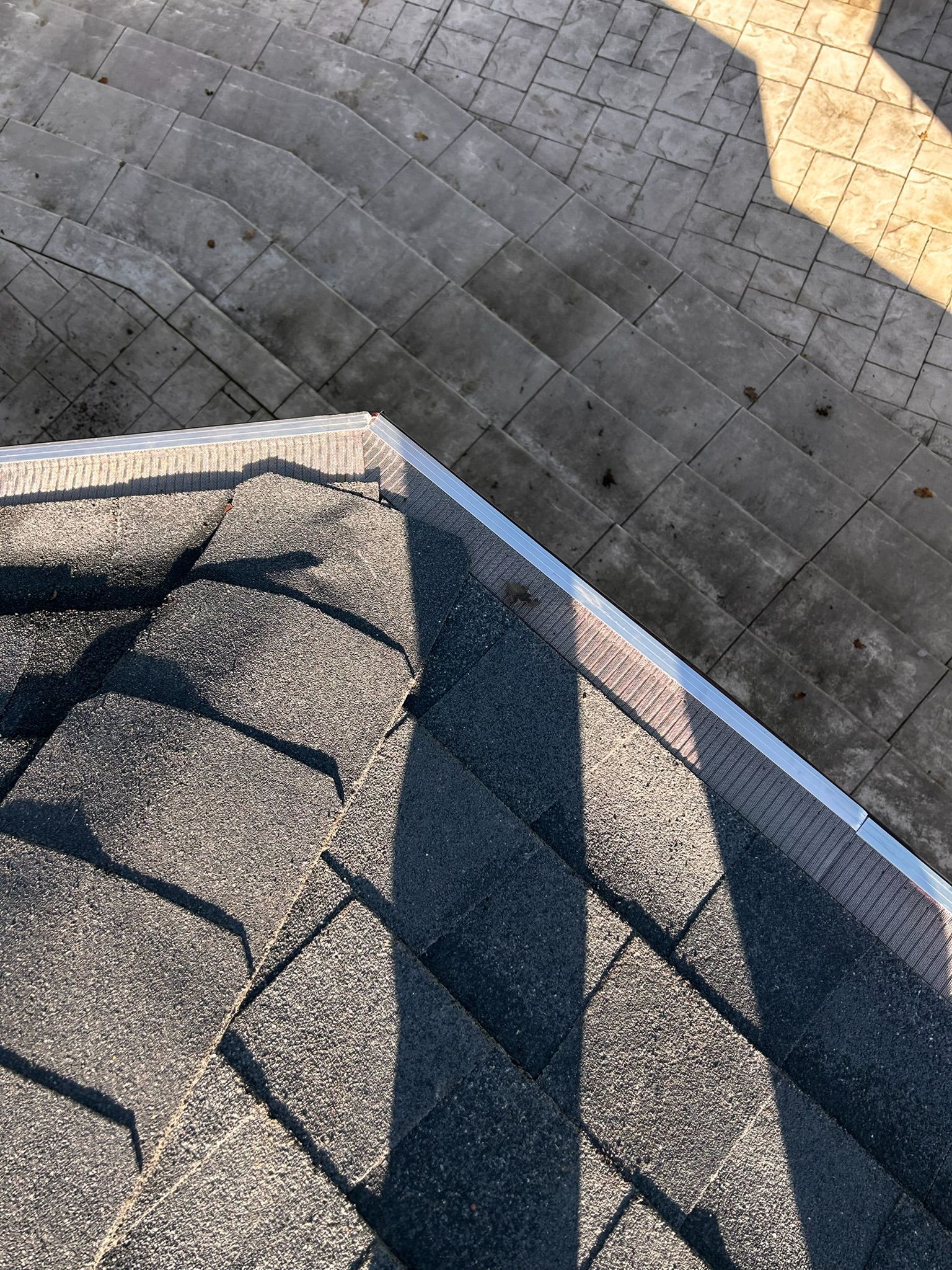 Overhead view of a roof with shingles and metal edging, with a gray concrete patio in the background.