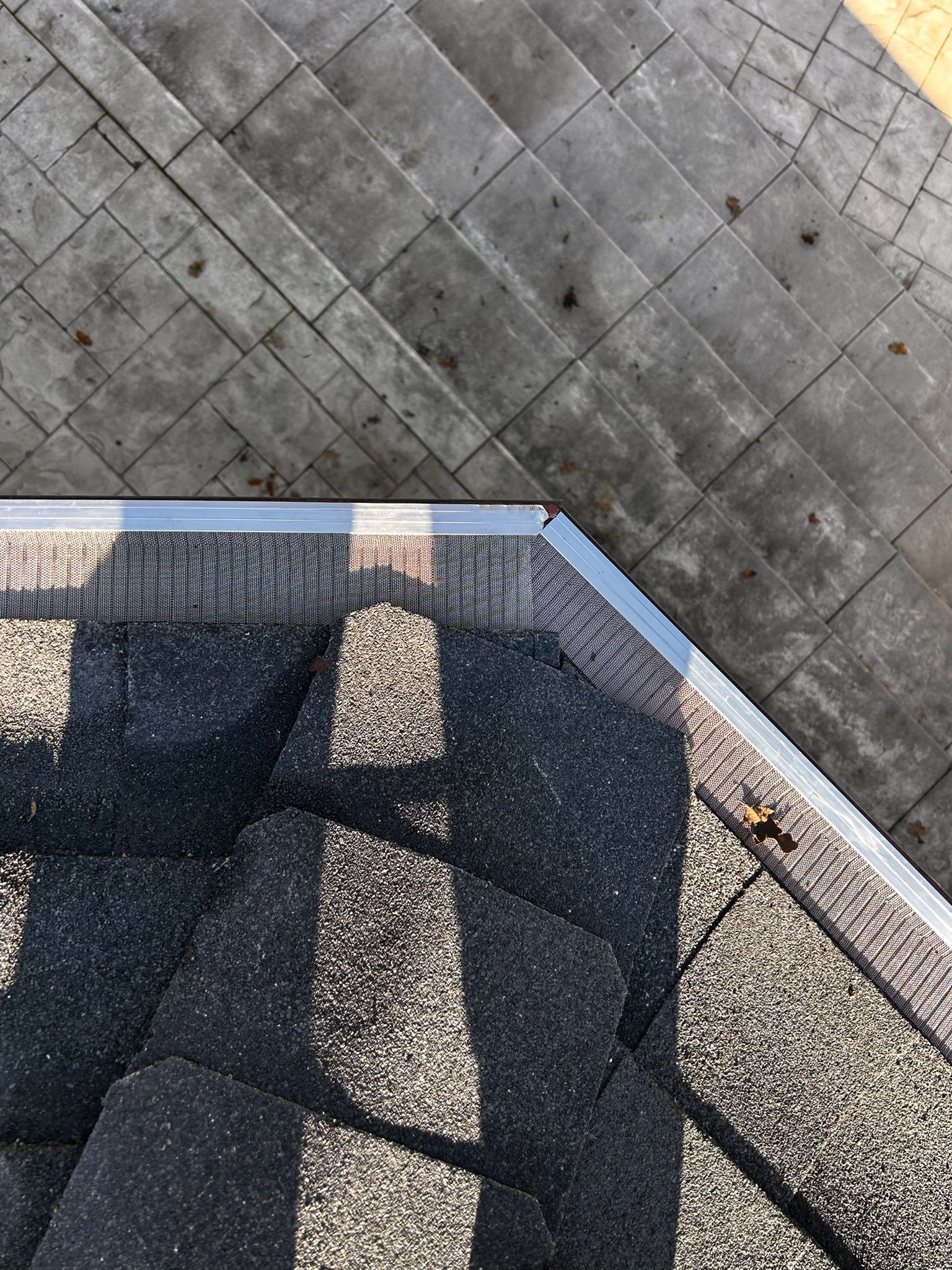 Overhead view of a roof edge meeting a brick or stone surface; dark shingles and light metal trim.