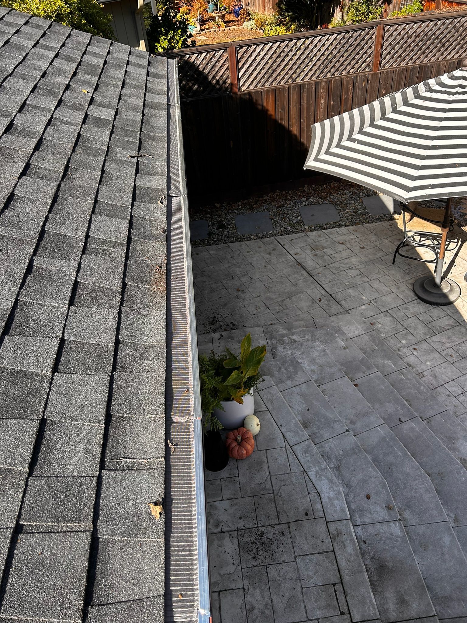 Overhead view of a roof with gray shingles, next to a backyard patio with a striped umbrella.