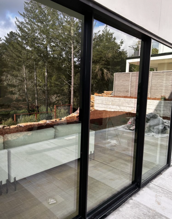 Black-framed sliding glass doors reflect an outdoor scene with trees and a building on a patio.