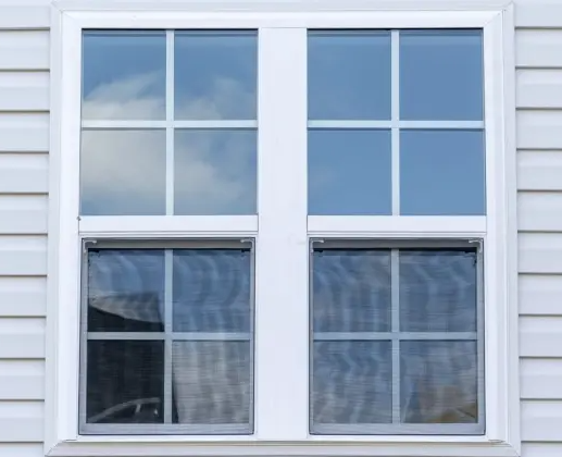 White framed double-hung window with a 6-pane upper section and a 4-pane lower section, on a light gray siding wall.