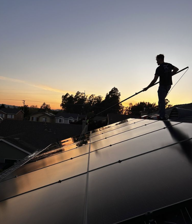 Person cleaning solar panels on a rooftop at sunset.