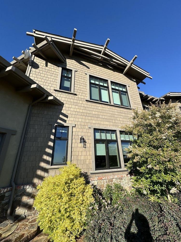 Exterior of a two-story house with shingle siding, dark-framed windows, and decorative roof beams, on a sunny day.