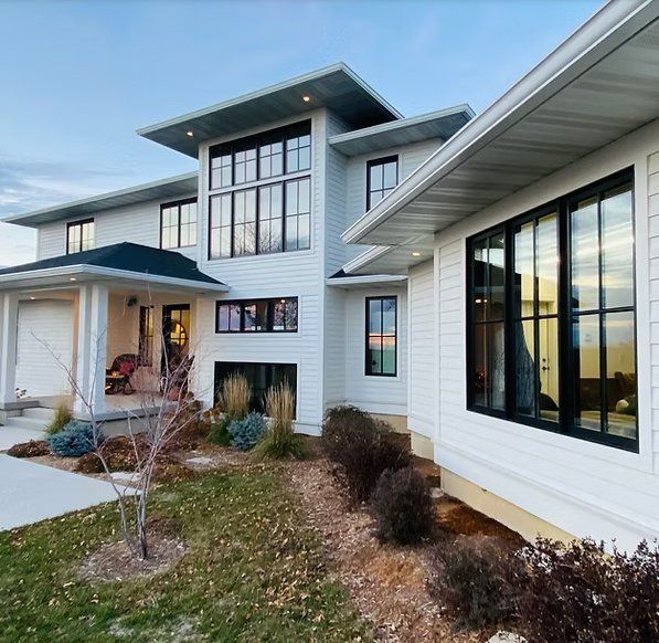White modern house with black-framed windows, surrounded by landscaping, under a blue sky.
