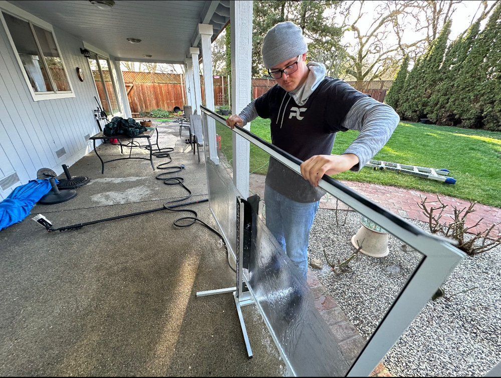 Man assembling a clear panel screen outdoors on a wet patio.