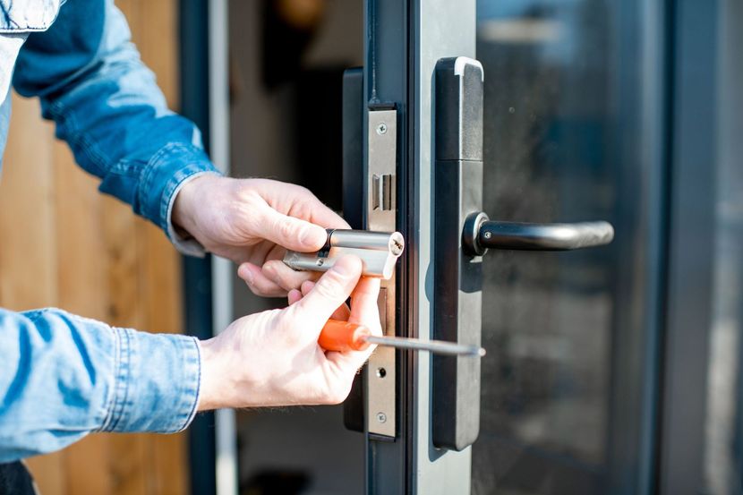 Person using a screwdriver to install a lock cylinder on a dark-framed glass door.