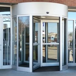 Glass doors with a silver frame, set in a stone building facade, with a wheelchair access sign on the left.