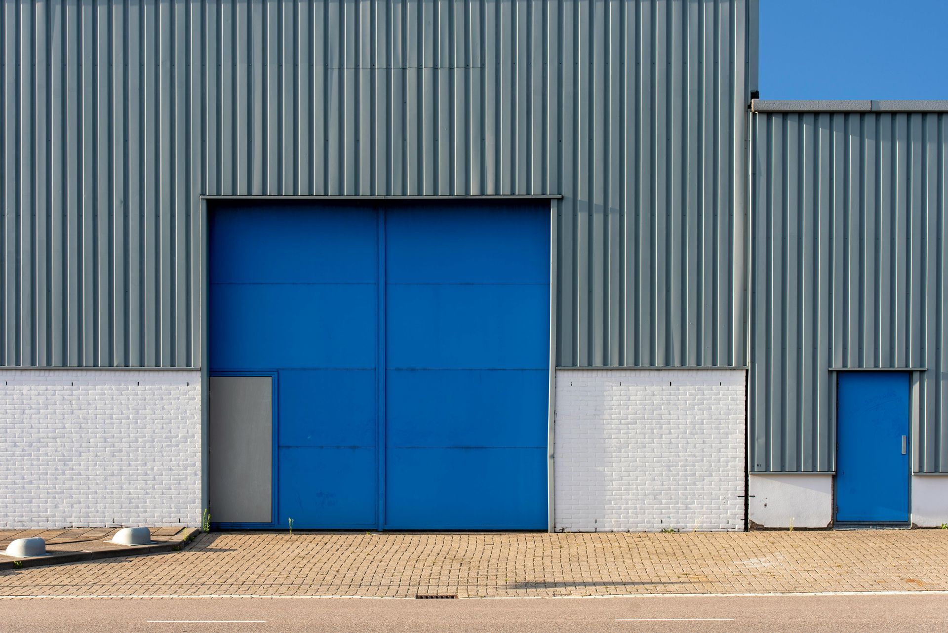 Blue warehouse doors in a gray industrial building with a small side door and gravel foreground
