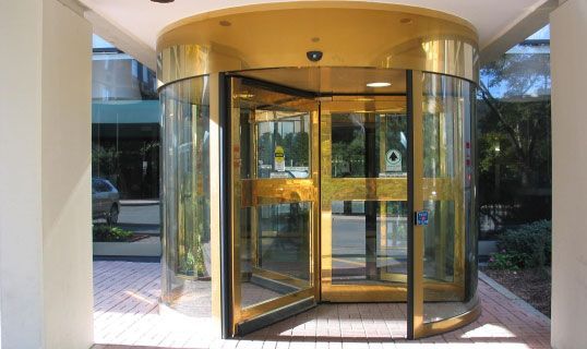 Modern commercial building with large glass windows reflecting trees and street; sunny day.