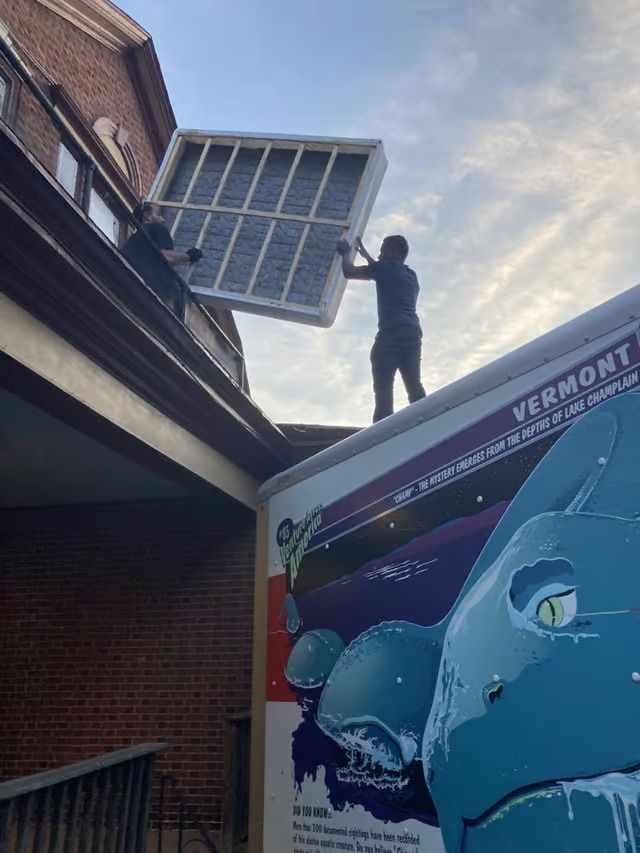 A man is standing on top of a truck holding a window.