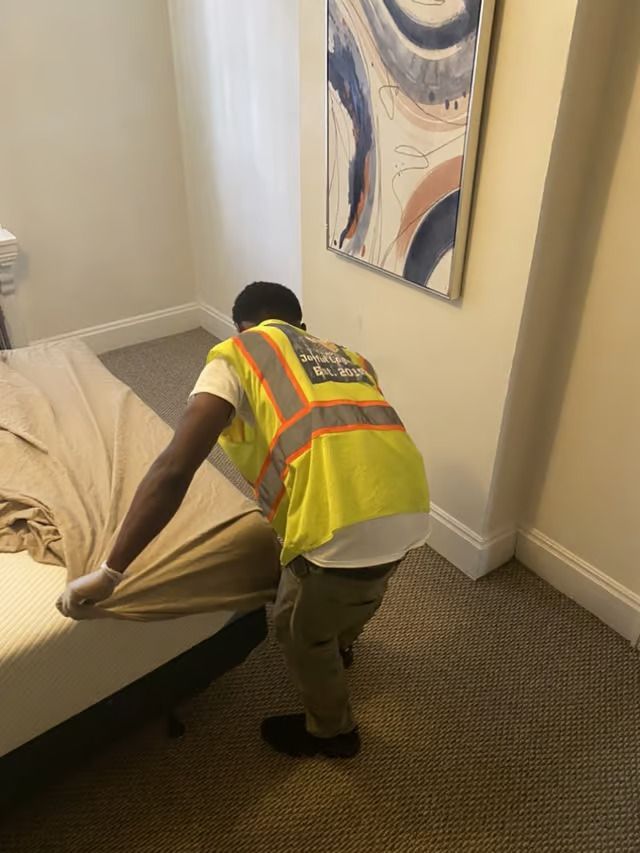 A man in a yellow vest is making a bed in a bedroom.