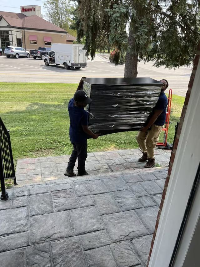 Two men are carrying a large piece of furniture on a porch.