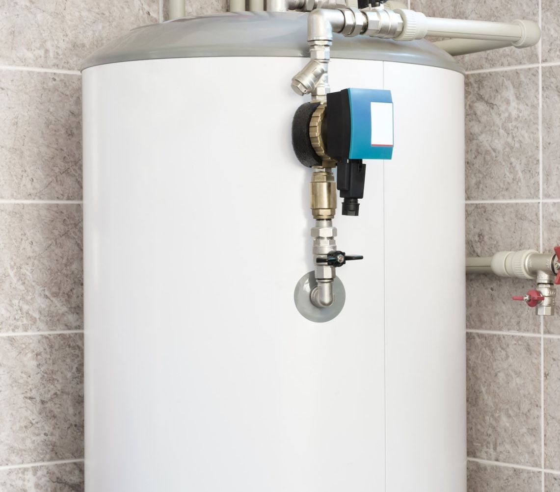 White water heater with pipes and a control box against tiled wall.