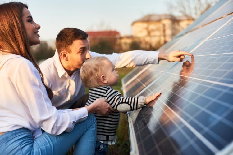 Side close-up shot of a young modern family with a little son getting acquainted with solar panel on a sunny day, green alternative energy