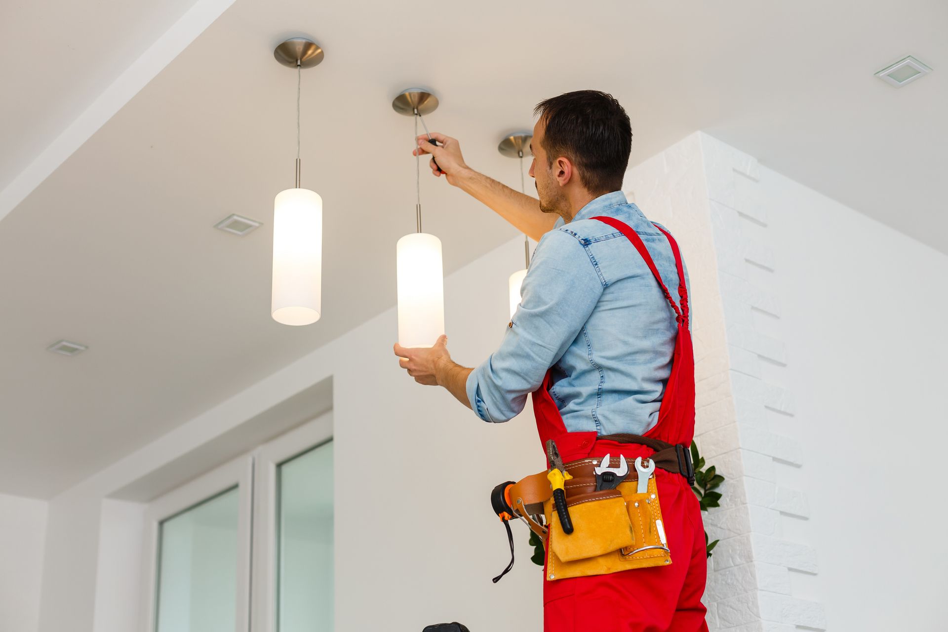 A man is installing a light fixture on the ceiling.