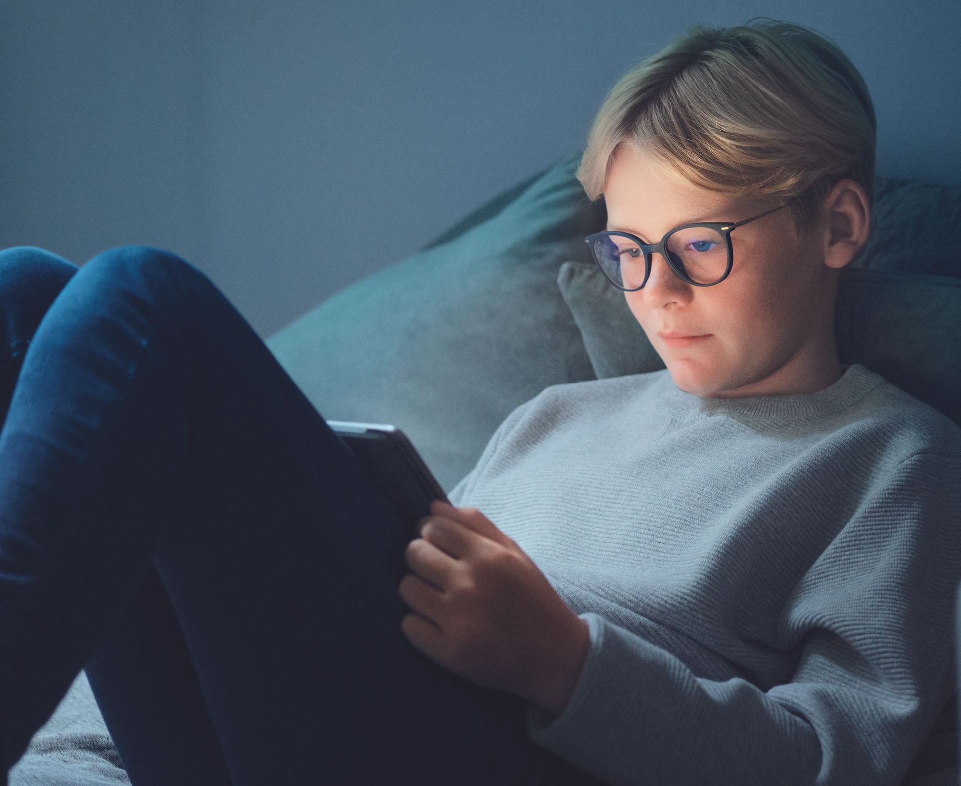 Ein Junge mit Brille sitzt auf einer Couch und benutzt ein Tablet . myopiekontrolle