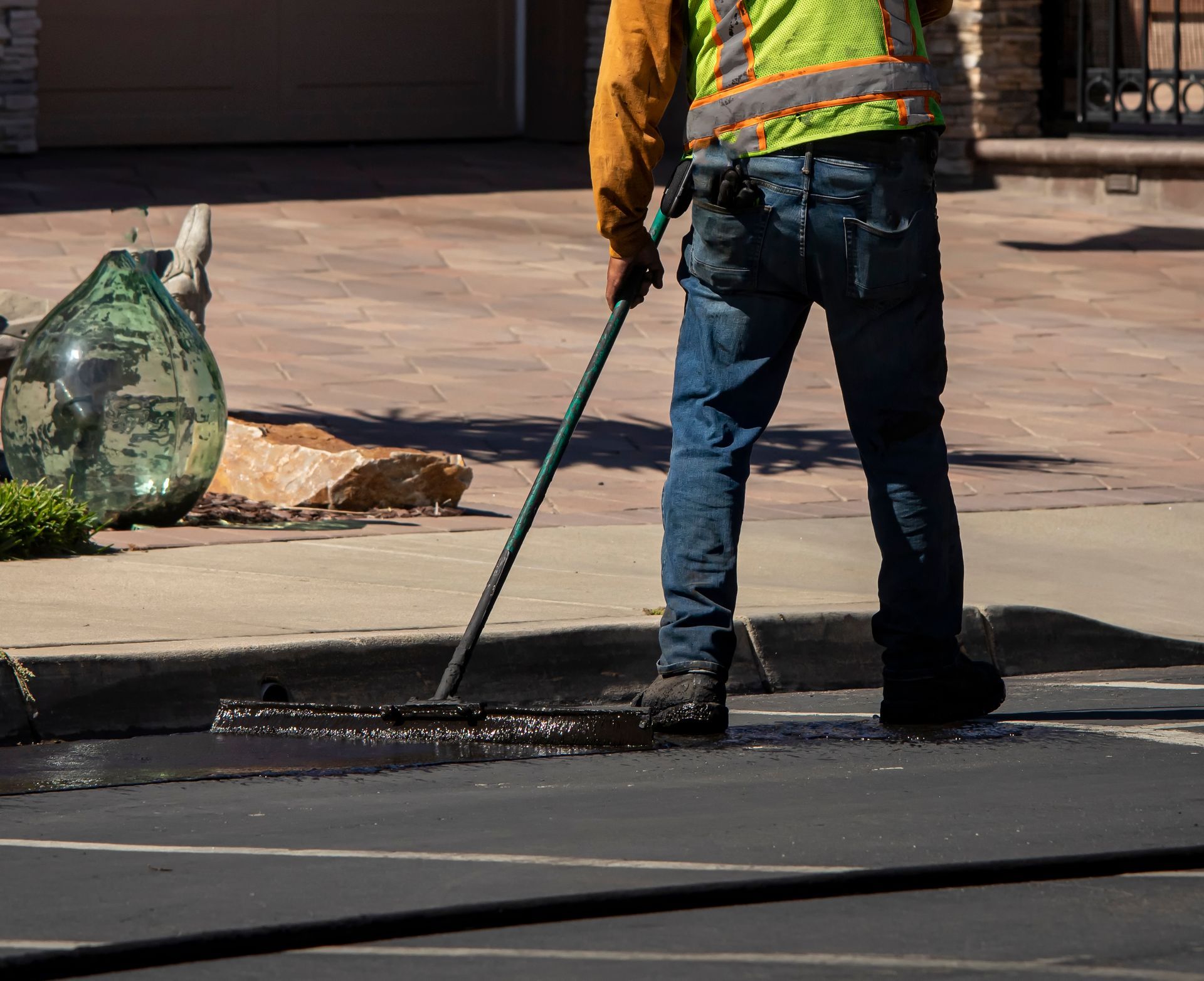 A man in a safety vest is cleaning a parking lot with a mop.