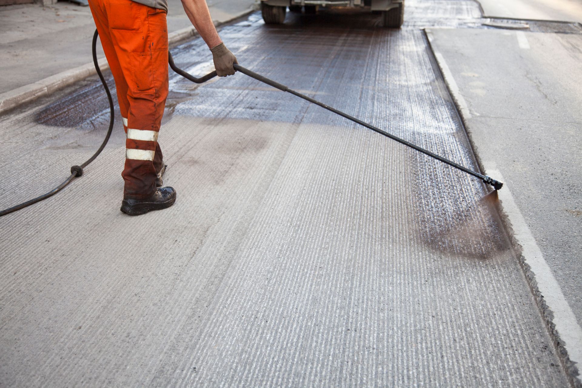 A man in orange pants is spraying asphalt on a street.