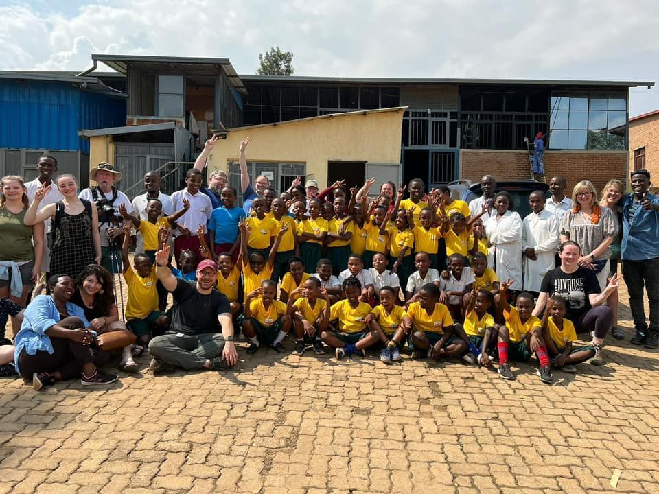 Group of children and adults in front of a building. Children wear yellow shirts, many people smile.