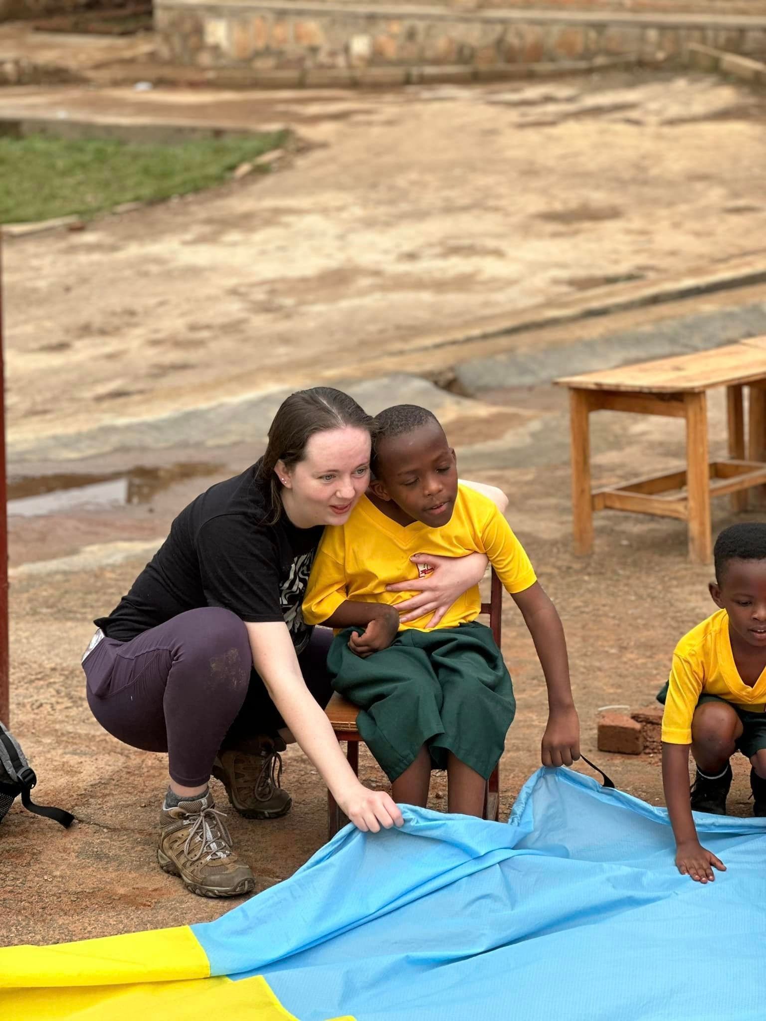 Woman and child in yellow shirt, playing with a blue and yellow tarp outdoors.