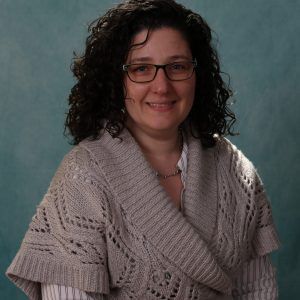 A woman wearing glasses and a sweater is smiling for the camera.