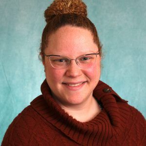 A woman wearing glasses and a red sweater is smiling for the camera.