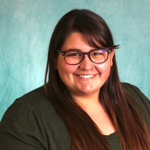 A woman wearing glasses and a green shirt is smiling for the camera.