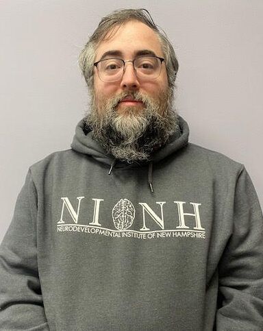 A man with a beard and glasses is wearing a gray hoodie.