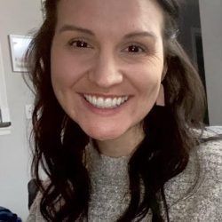 A woman is smiling for the camera while wearing a sweater and earrings.