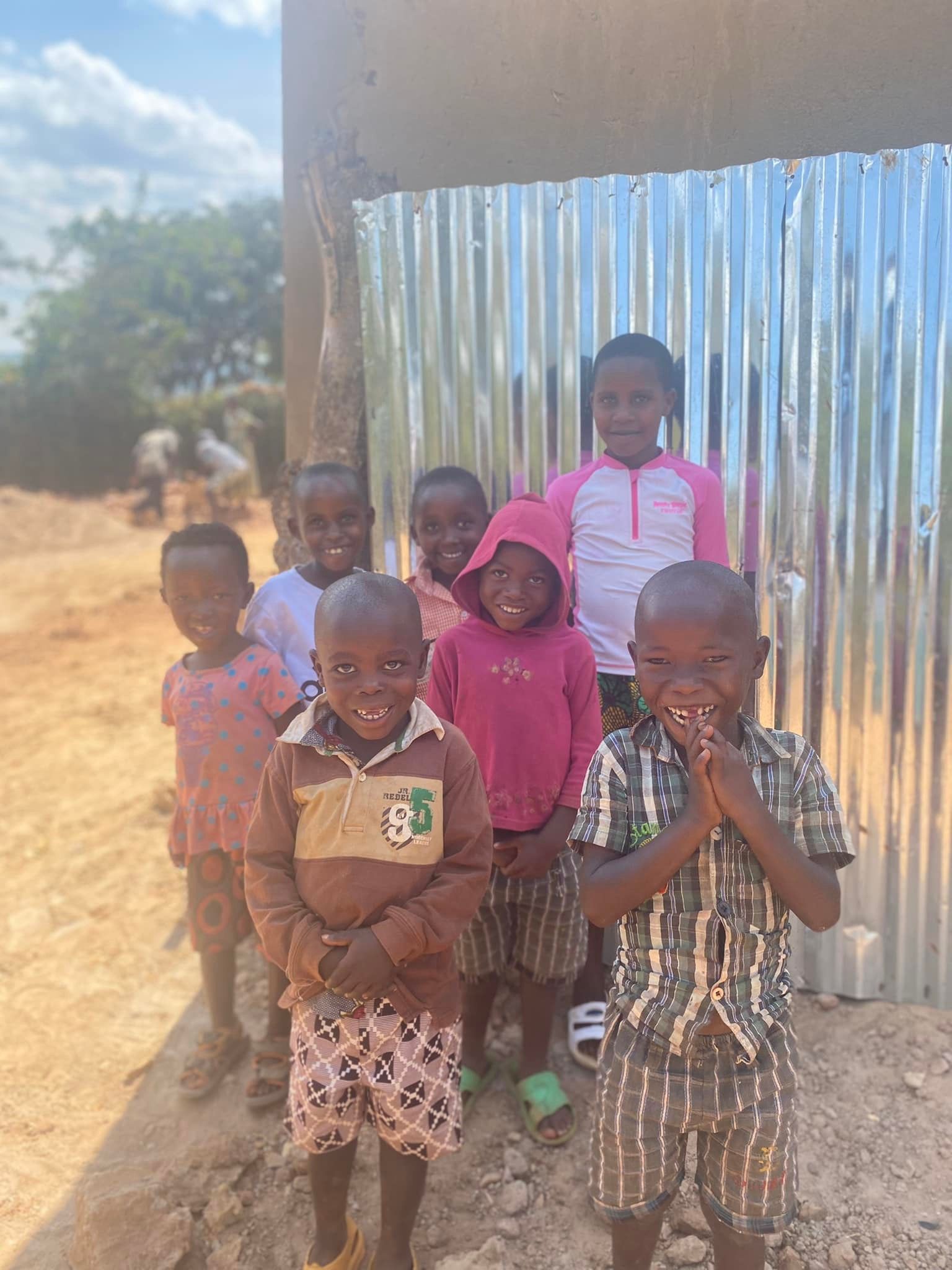 A group of children are standing next to each other on a dirt road.