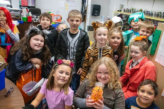 A group of children dressed in costumes are posing for a picture in a classroom.