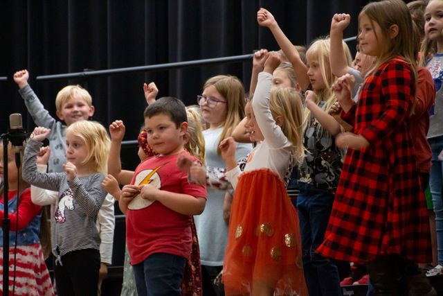 A group of children are standing on a stage with their hands in the air.