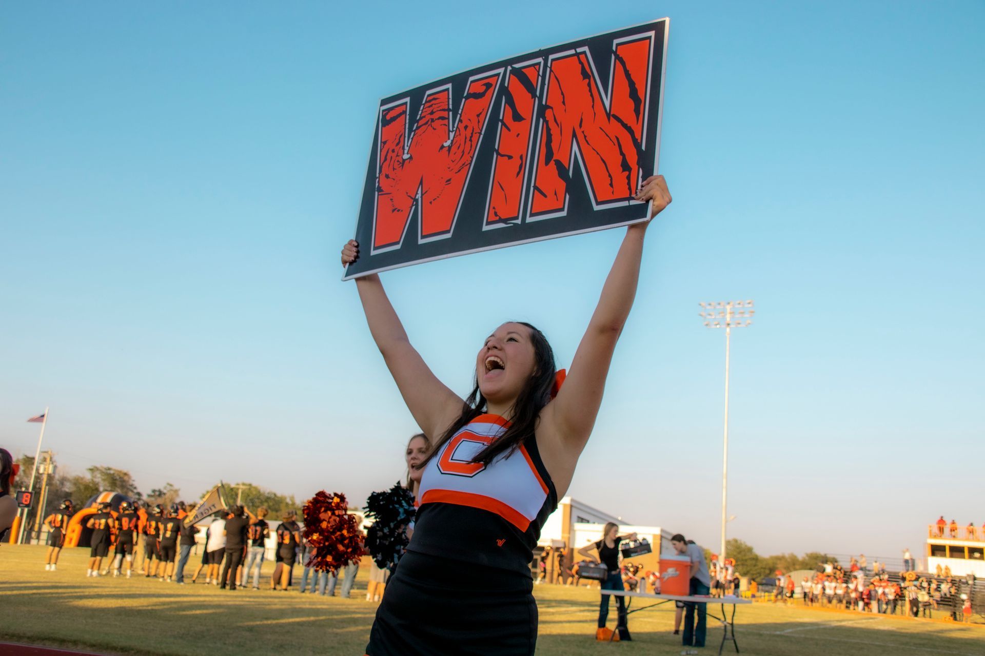 A cheerleader is holding a sign that says win in the air.