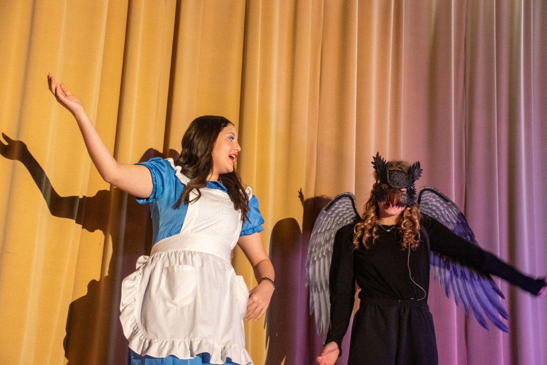 A woman in a blue dress is standing next to a woman in a black dress with wings on a stage.