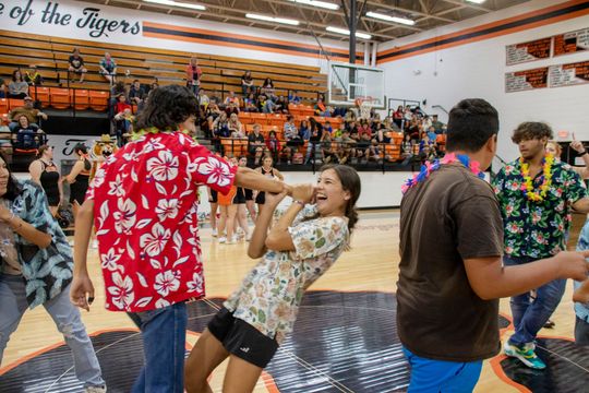 A group of people in hawaiian shirts are dancing in a gym.