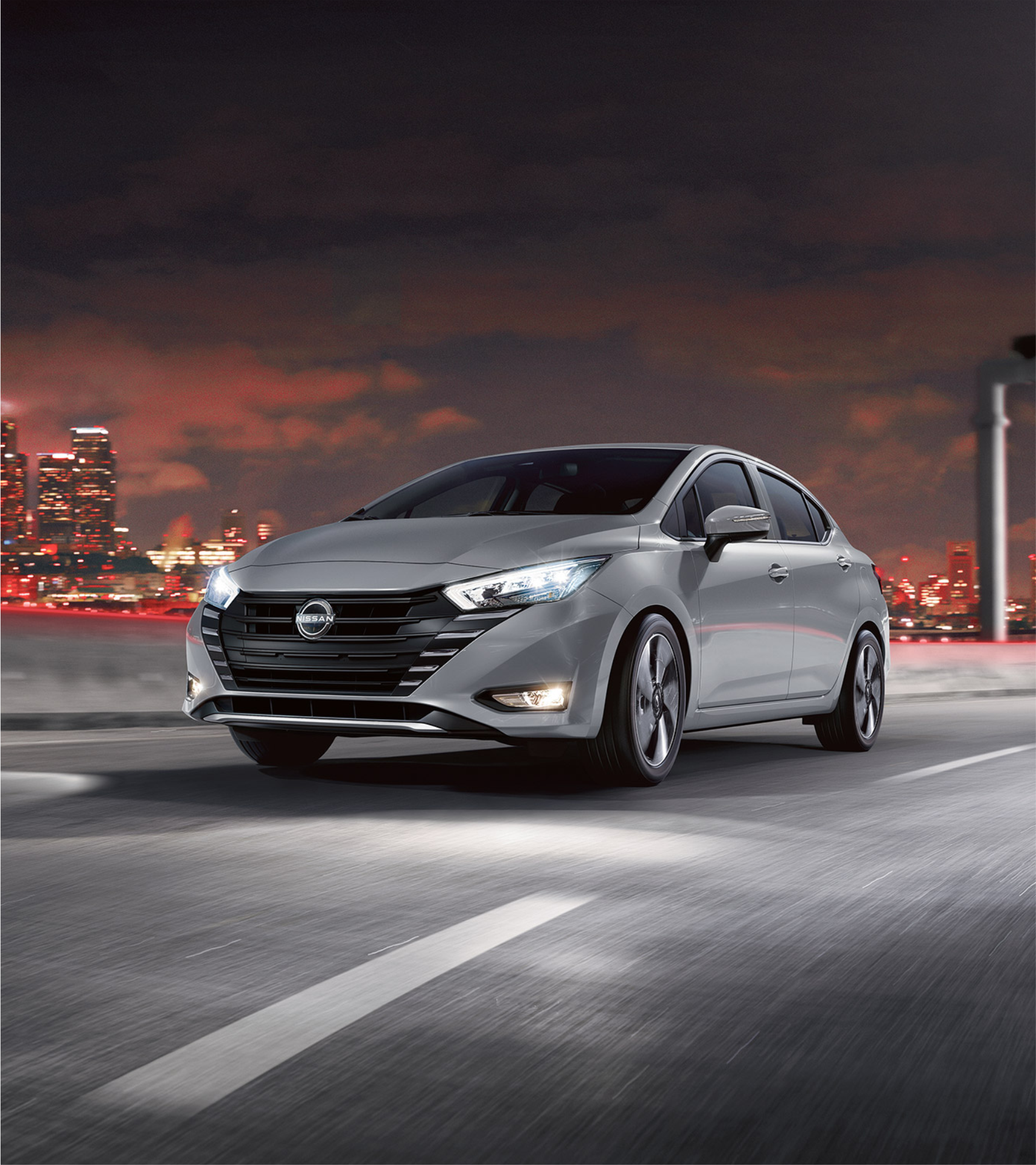 Um carro prateado passa por uma rua da cidade à noite.