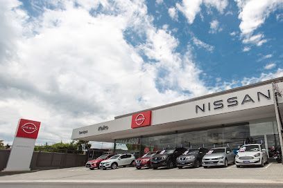 Exterior de uma concessionária Nissan com carros estacionados sob um céu parcialmente nublado.