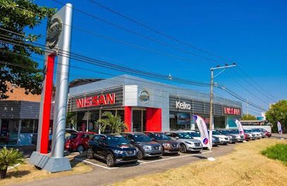 Concessionária Nissan com fileiras de veículos sob um céu azul brilhante.